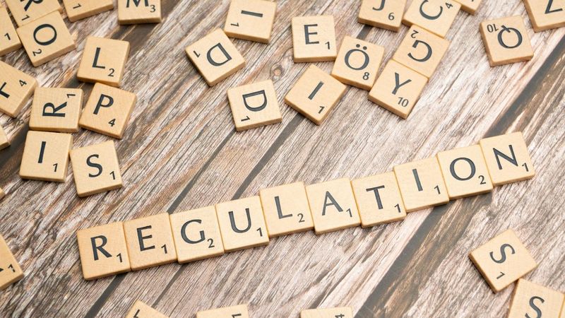 Buchstaben-Spielsteine bilden das Wort Regulation auf Holzuntergrund, KI-Regulierung Mittelstand 2026