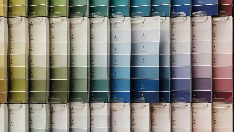 Wand mit hunderten Farbkarten in einem geordneten Raster, sortiert von Grün über Blau zu Lila