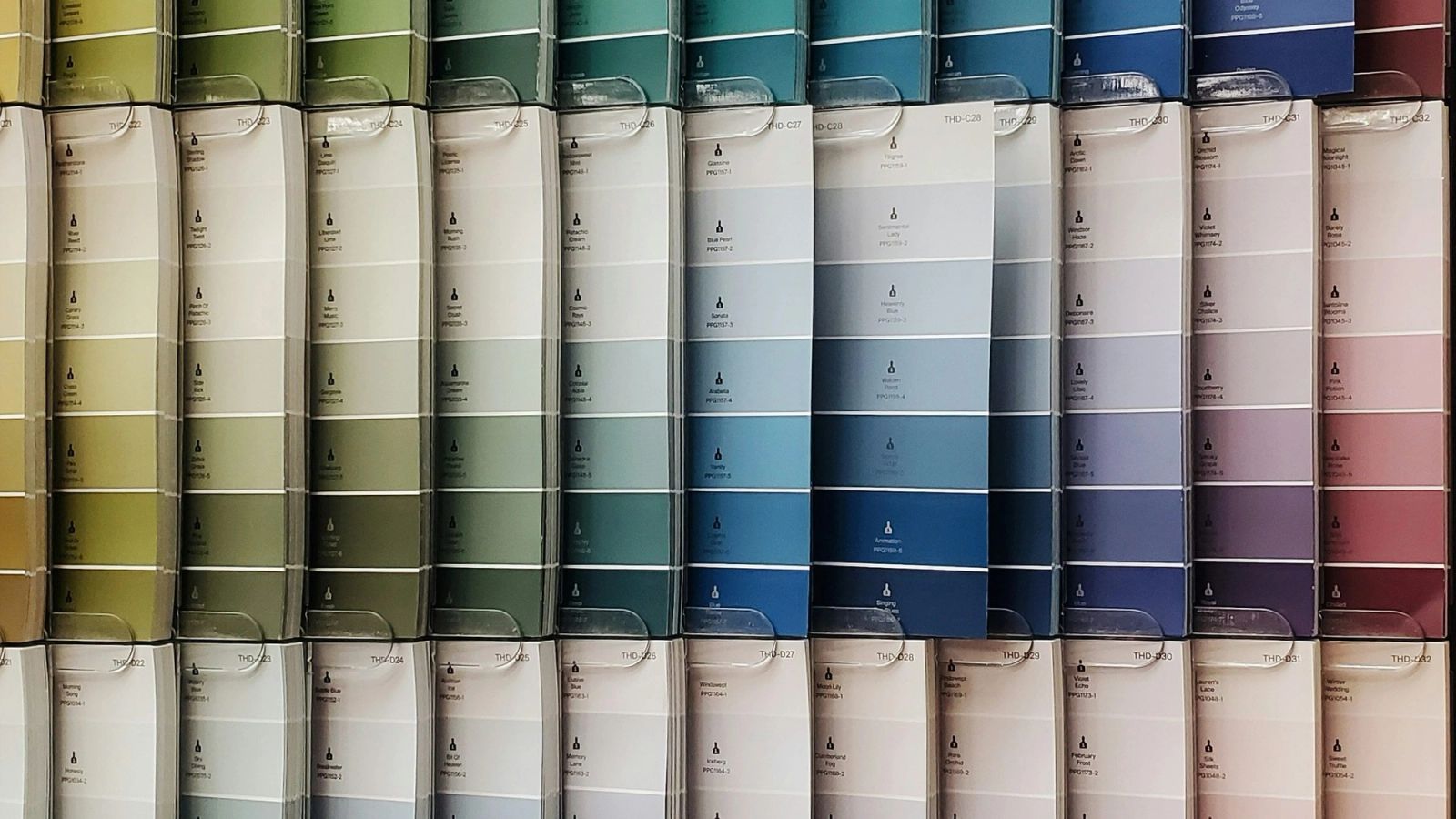 Wall covered with hundreds of paint sample cards in an ordered grid, sorted from green through blue to purple