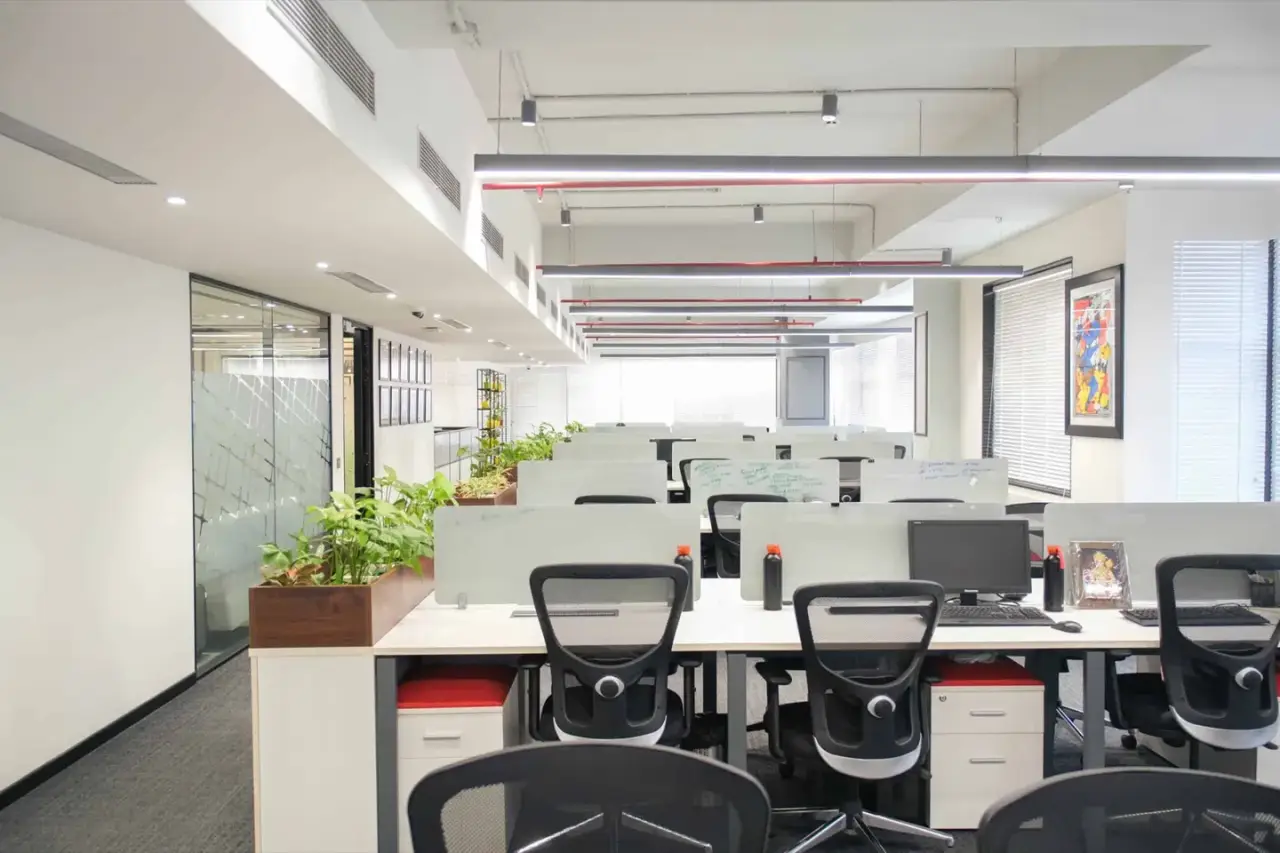 Rows of white workstations with mesh chairs and a planter divider on an open office floor, in an AIHP managed office in Gurgaon