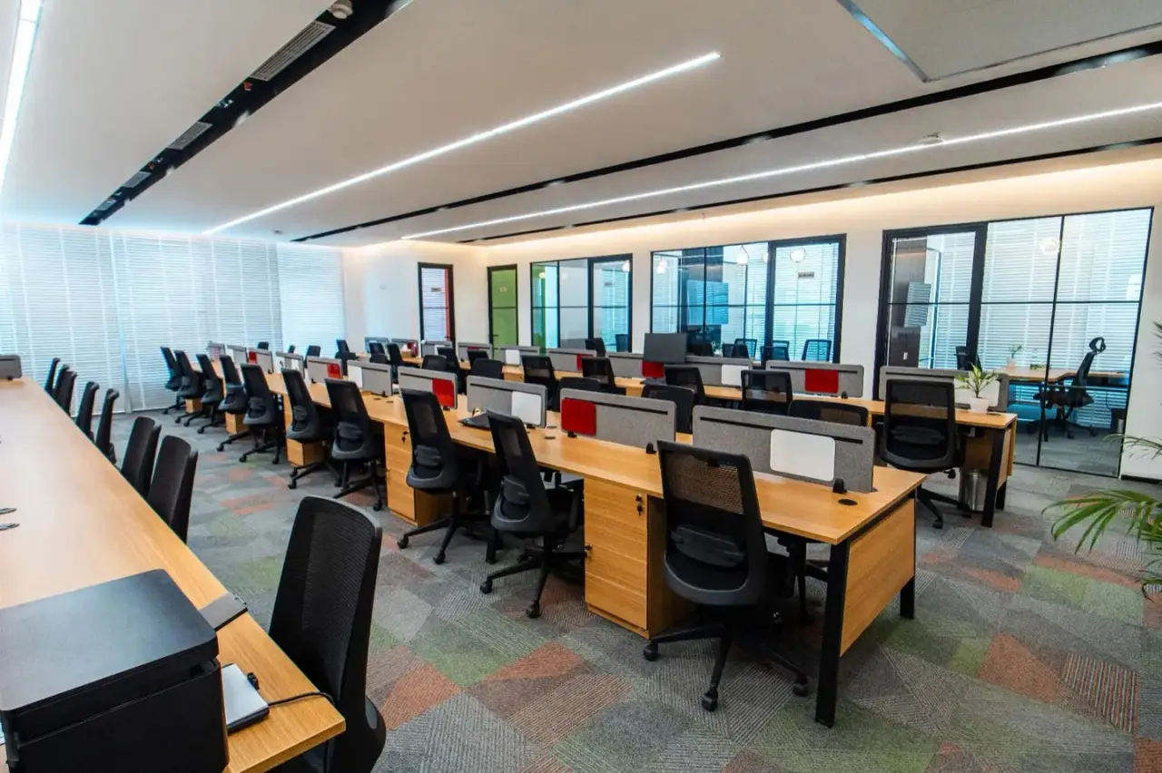 Rows of wood-topped workstations along a glass wall of cabins, in an AIHP managed office in Gurgaon