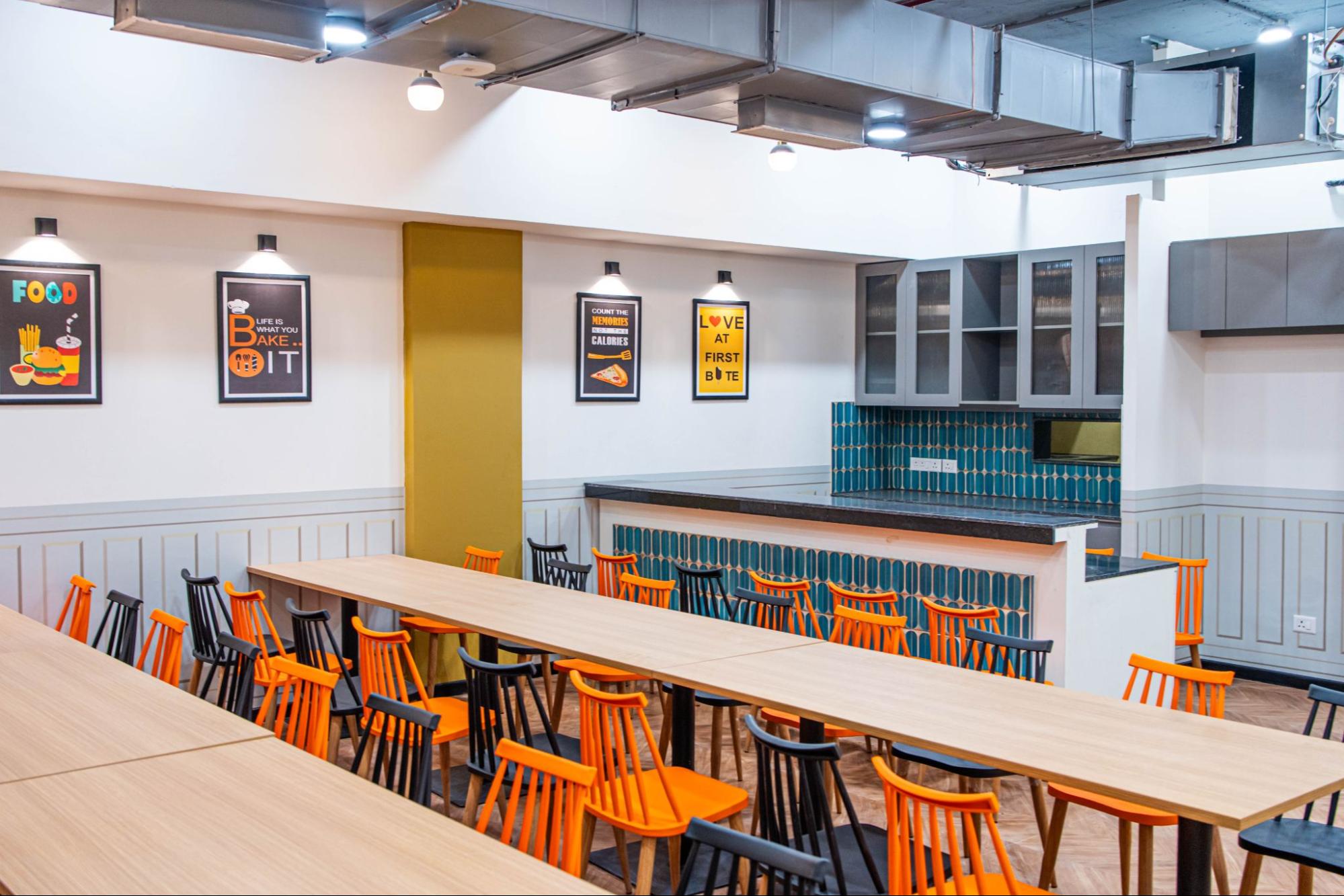 Pantry and dining area with long wooden tables, orange and black chairs and a tiled counter, AIHP SCO 34, Sector 32 Gurgaon