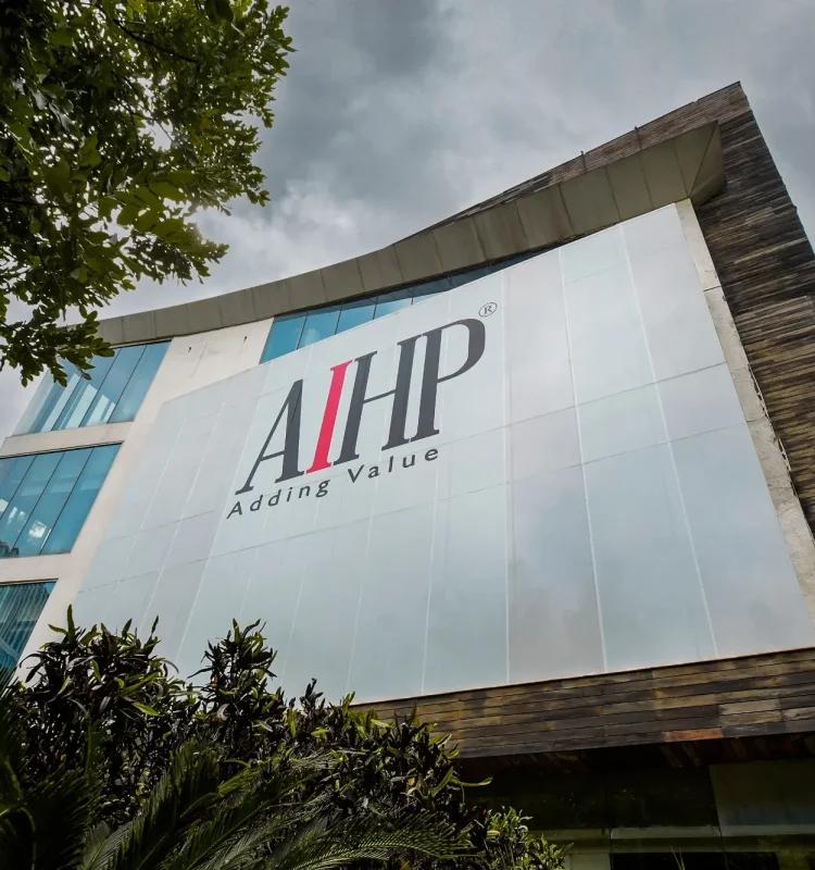 Upward view of white AIHP-branded facade with curved corner and stone trim, AIHP Broadway, Sector 32 Gurgaon