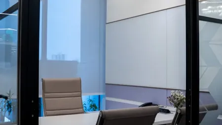 Glass-walled meeting room with a small desk and two guest chairs, seen through an open door