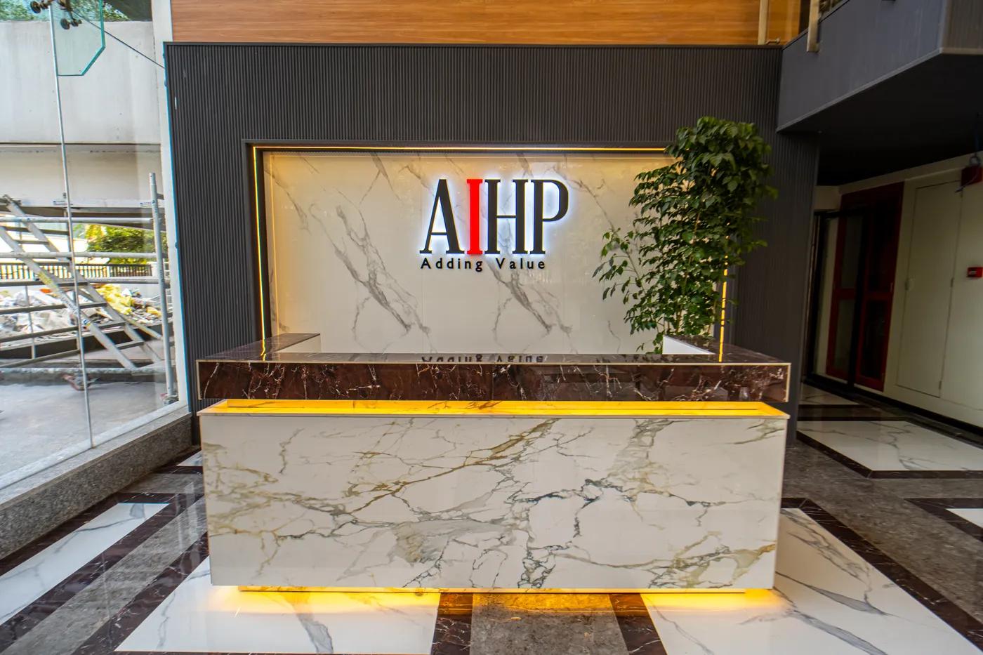 AIHP Atrium reception desk with backlit marble brand wall and the AIHP 'Adding Value' logo, Sector 32 Gurgaon