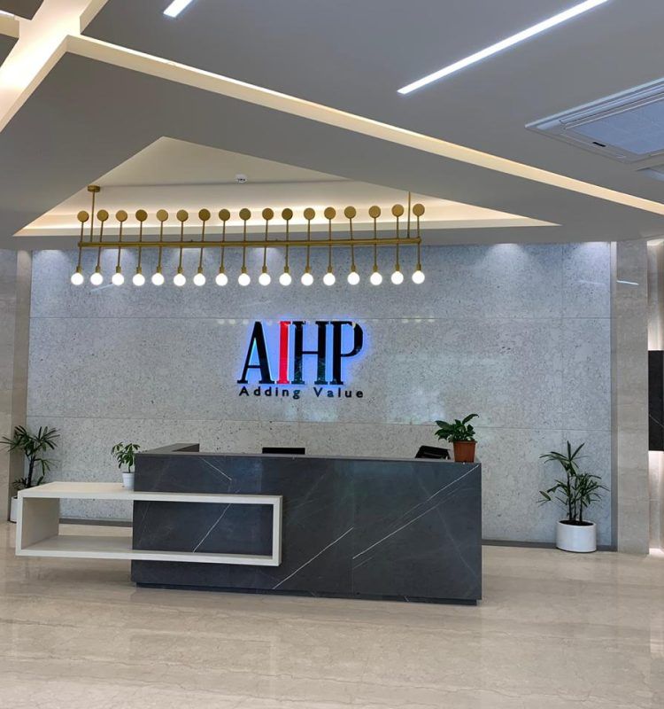 Reception desk with illuminated AIHP logo and gold pendant lighting at AIHP Palms