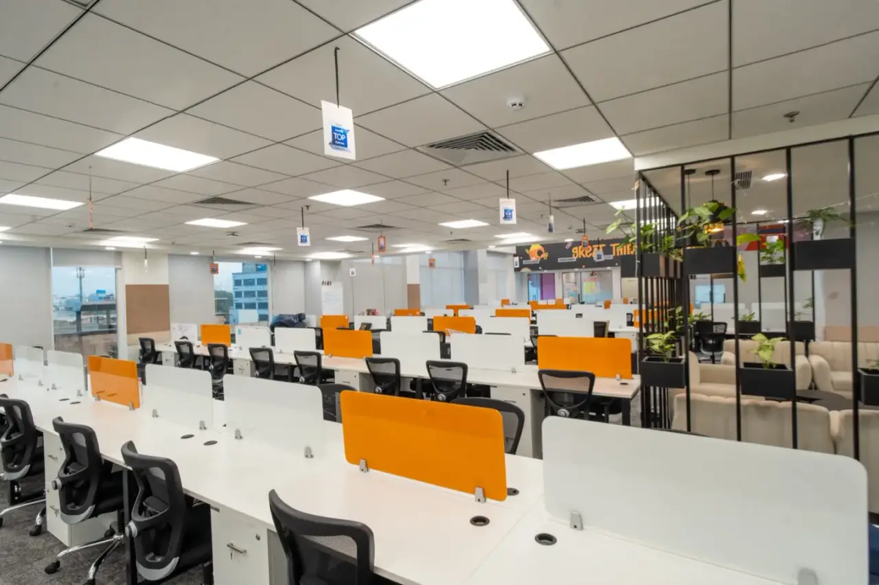 Long rows of white workstations with orange divider panels and a glass cabin to one side, in an AIHP managed office in Gurgaon