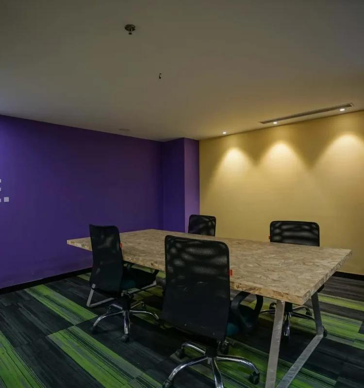 Small huddle meeting room with purple and mustard accent walls, OSB-top table and mesh chairs, AIHP Horizon, Udyog Vihar Gurgaon