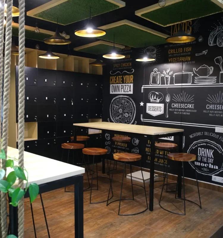 Cafe corner with chalkboard menu mural, high stools, wood counter and black storage lockers, AIHP Horizon, Udyog Vihar Gurgaon