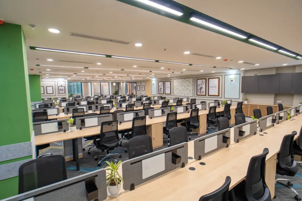 AIHP Atrium open-plan workstation floor with rows of desks and green accent walls, Sector 32, Gurgaon