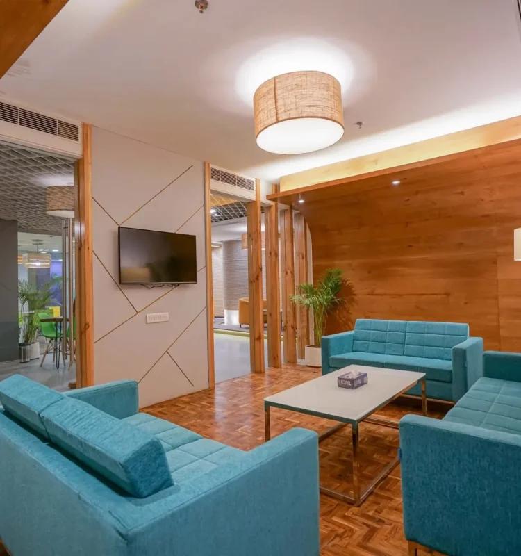 Lounge with teal sofas, wood-paneled wall, wall-mounted TV, and potted plants
