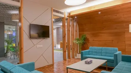 Lounge with teal sofas, wood-paneled wall, wall-mounted TV, and potted plants