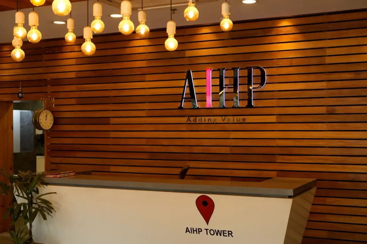 Reception with a marble desk in front of a wood-slatted wall carrying the AIHP logo, in an AIHP managed office in Gurgaon