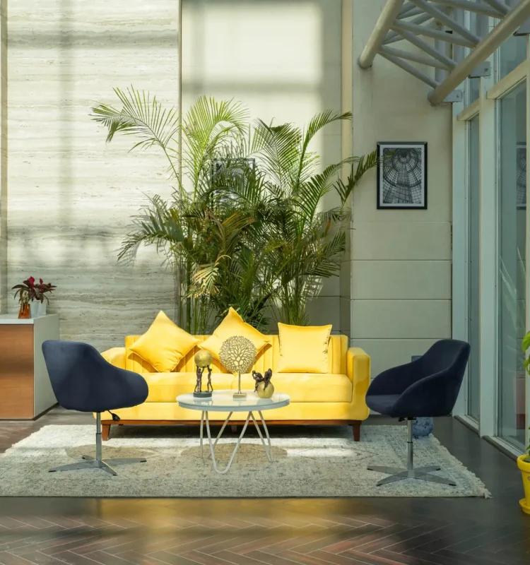 Yellow sofa and navy swivel chairs under a skylit atrium with palms, AIHP Executive Center, Sector 32 Gurgaon