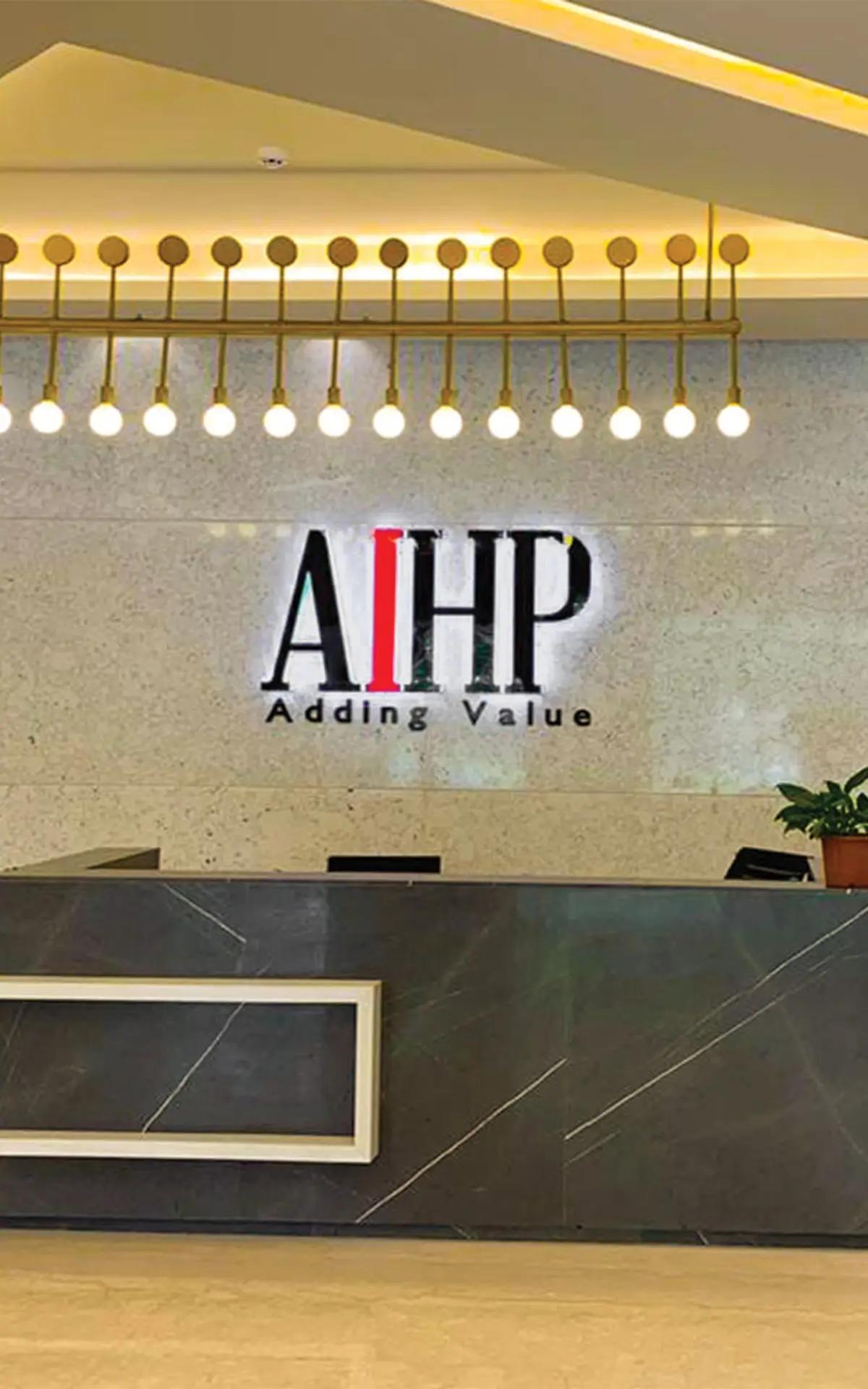 Reception desk with backlit AIHP Adding Value logo on stone wall and gold pendant globe lights, AIHP Palms, Udyog Vihar Gurgaon