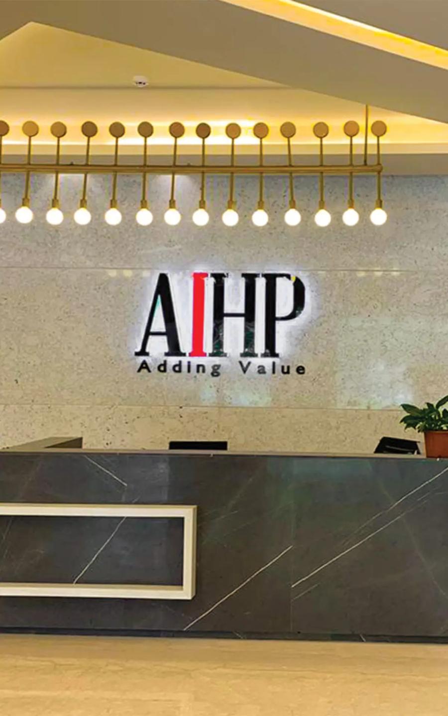 Reception desk with backlit AIHP Adding Value logo on stone wall and gold pendant globe lights, AIHP Palms, Udyog Vihar Gurgaon
