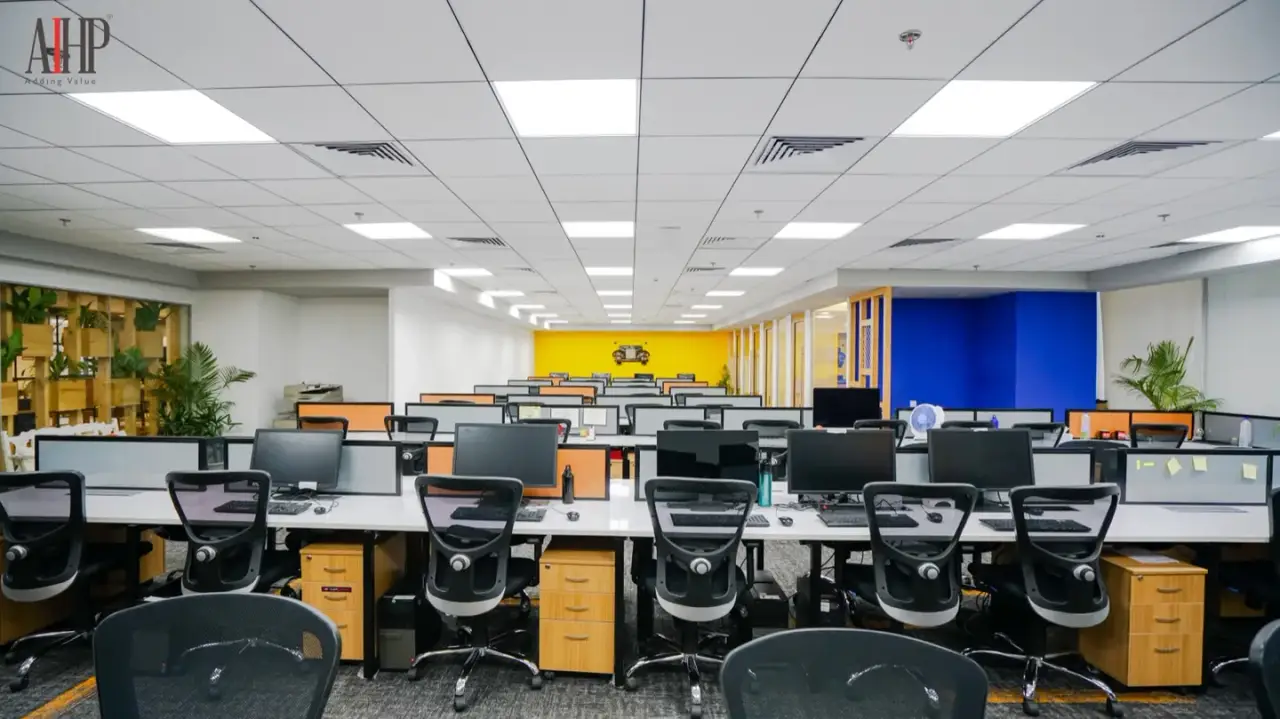 Wide open-plan floor of workstation rows with a yellow and blue feature wall at the far end, in an AIHP managed office in Gurgaon