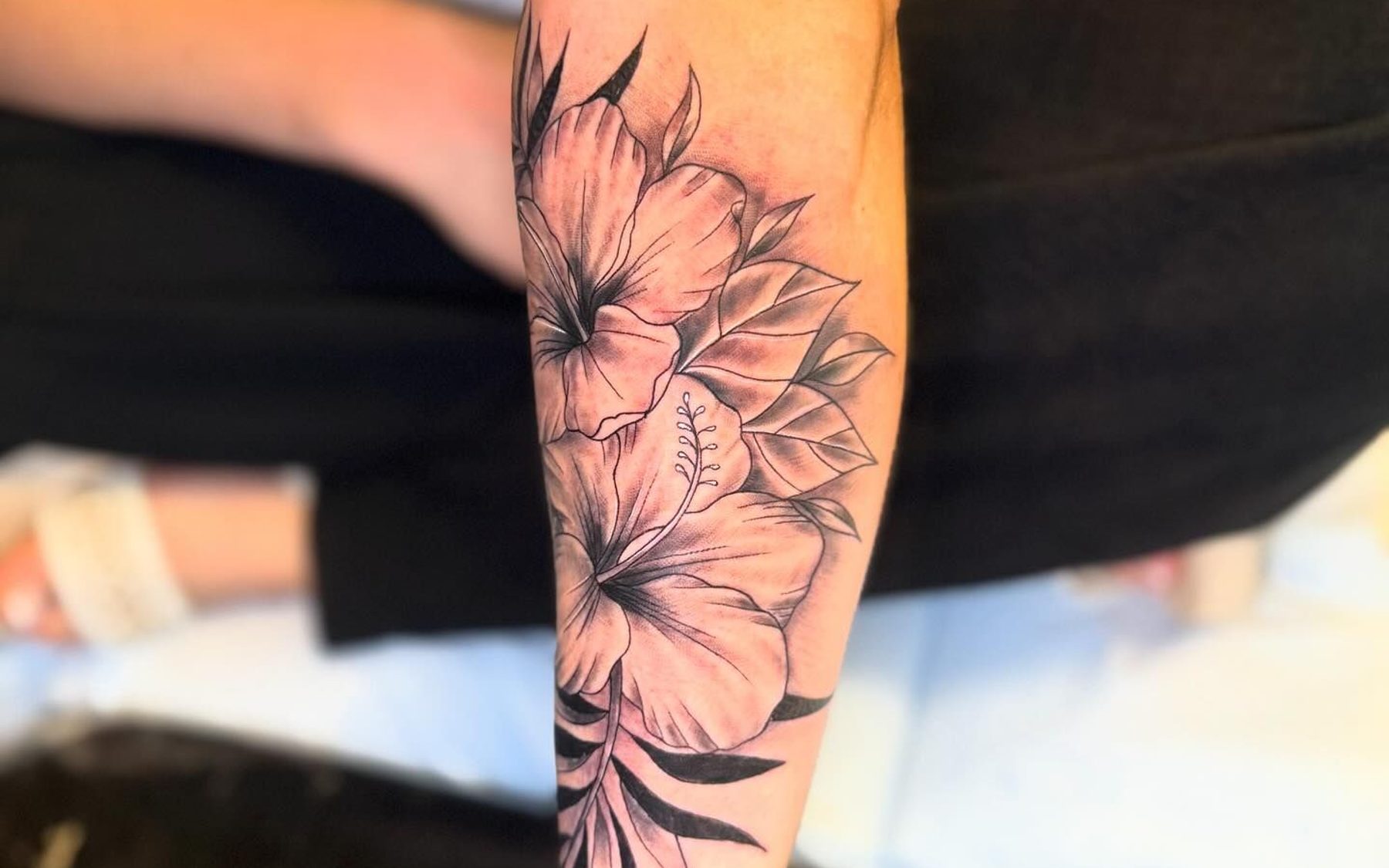 Detailed botanical forearm piece featuring hibiscus flowers and foliage in black and grey
