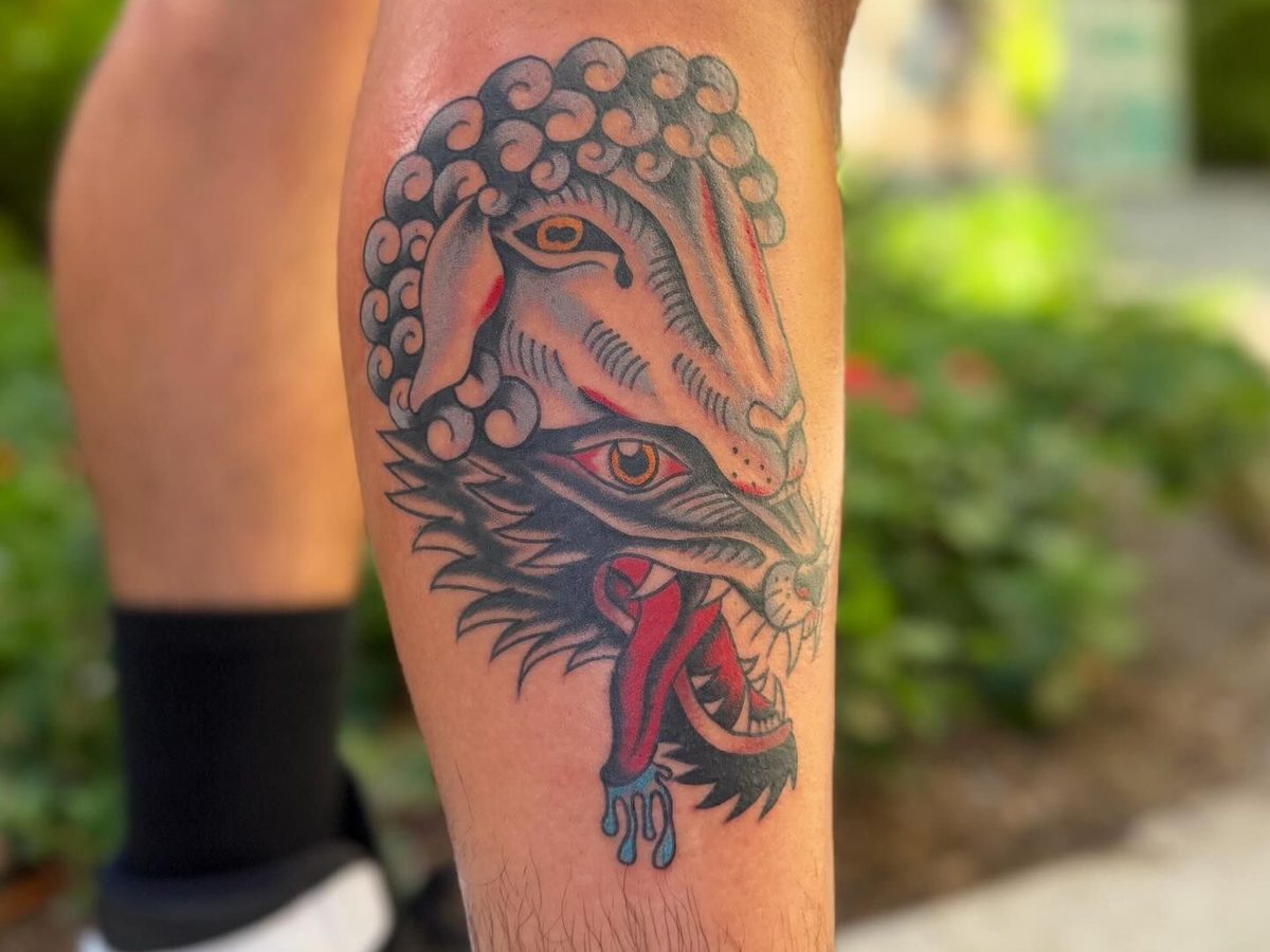 Bold traditional calf piece featuring intertwined wolf and ram heads with classic bold linework and limited color palette