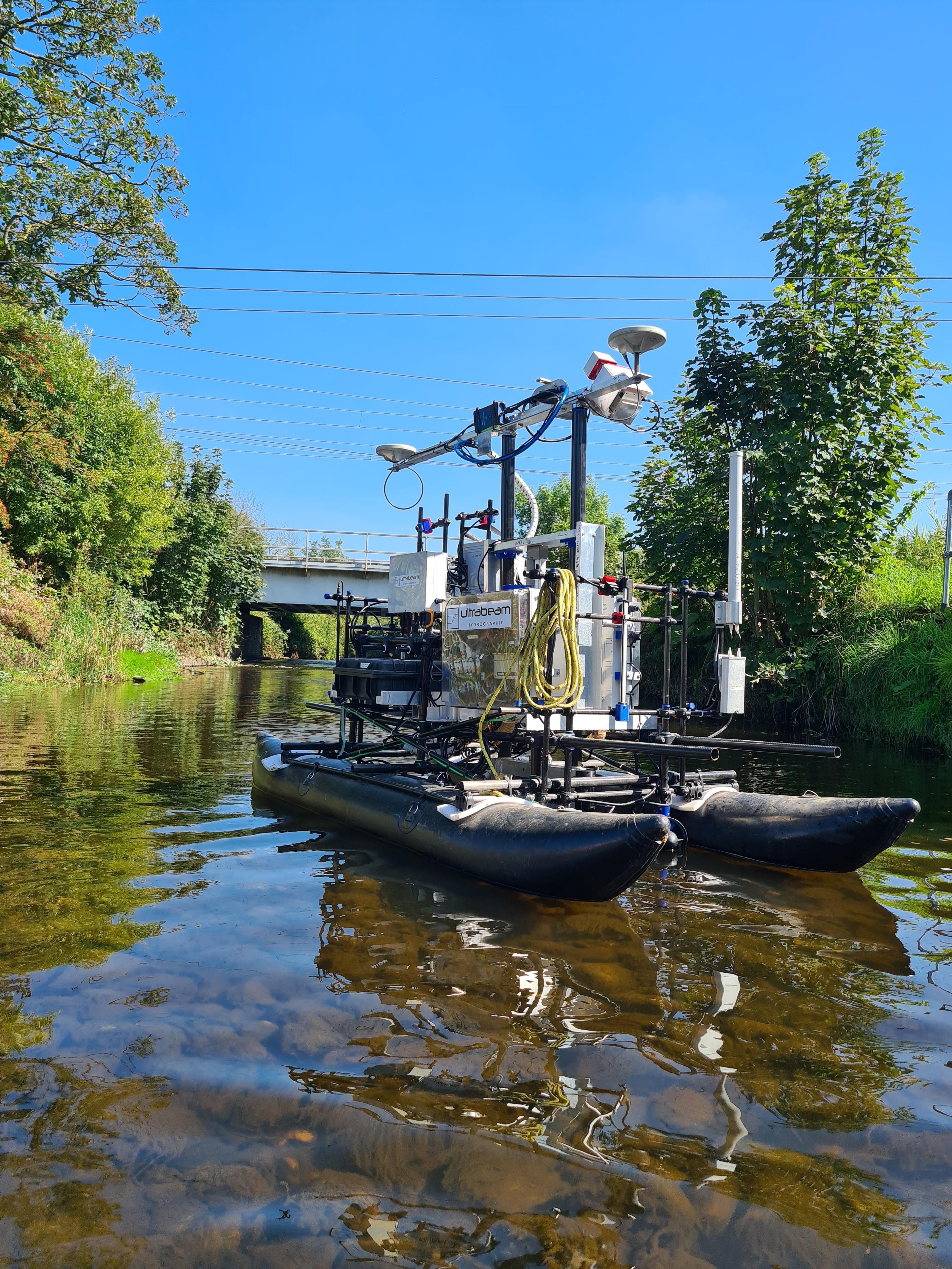 A doubled hulled uncrewed survey craft on a rive with a bridge in the background