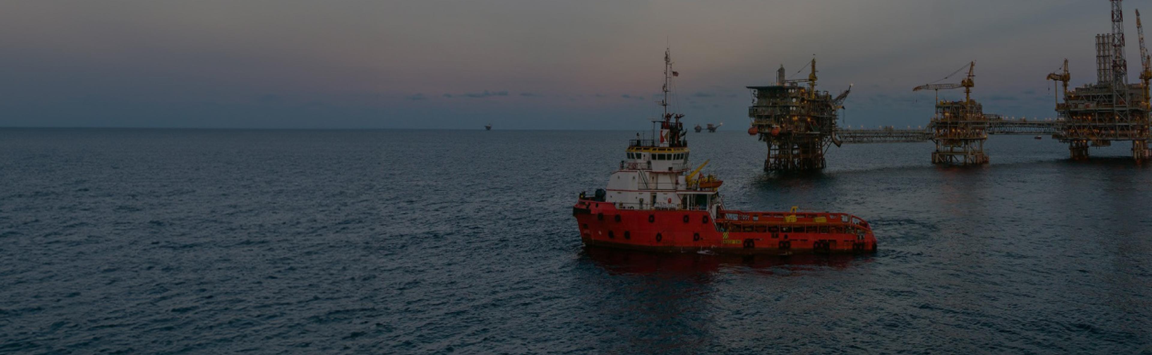An offshore vessel sailing with an oil platform visible in the background