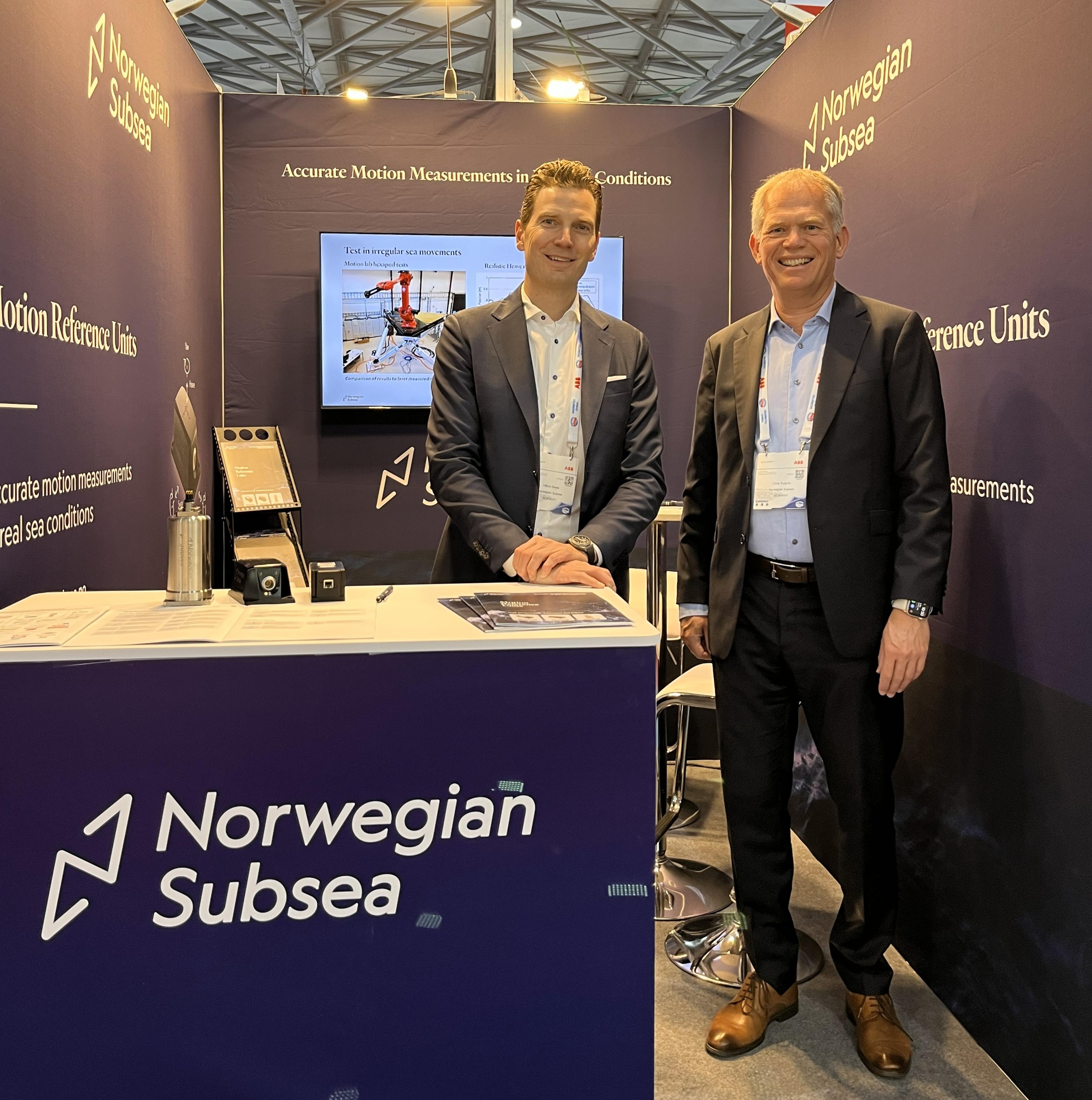 Two men in suits stood on an exhibition booth with blue walls