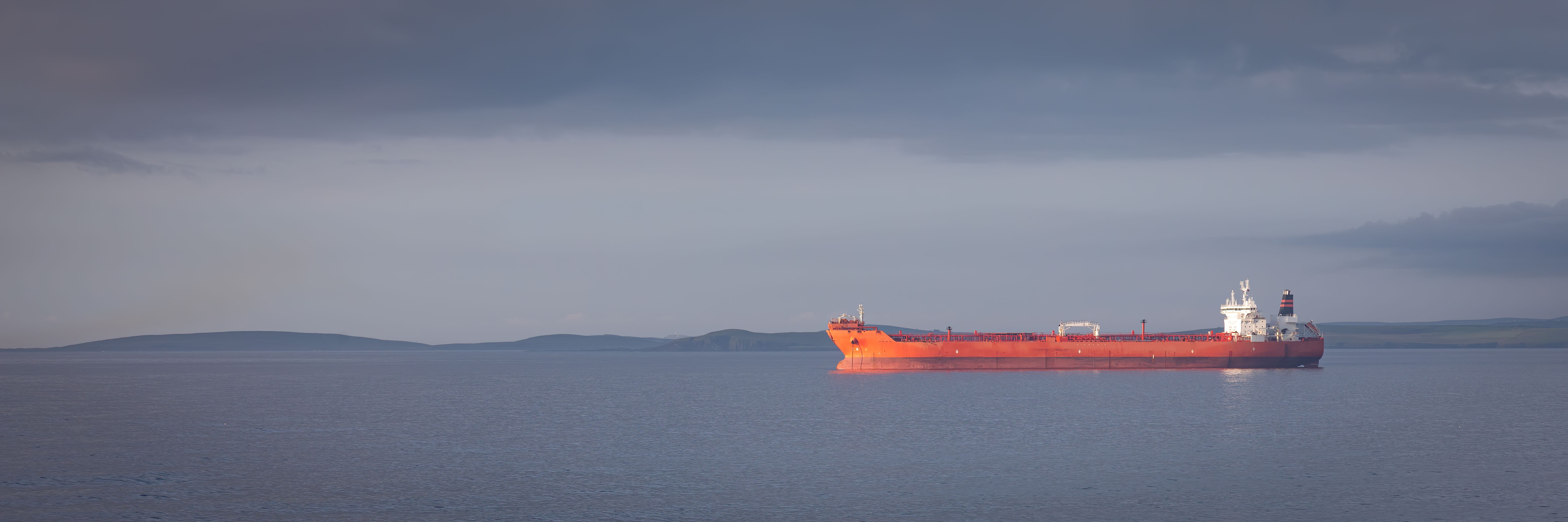 An offshore vessel sailing with an oil platform visible in the background