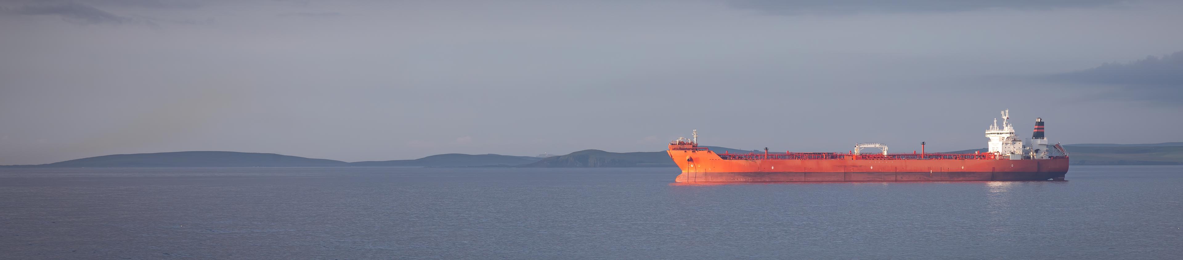 An offshore vessel sailing with an oil platform visible in the background