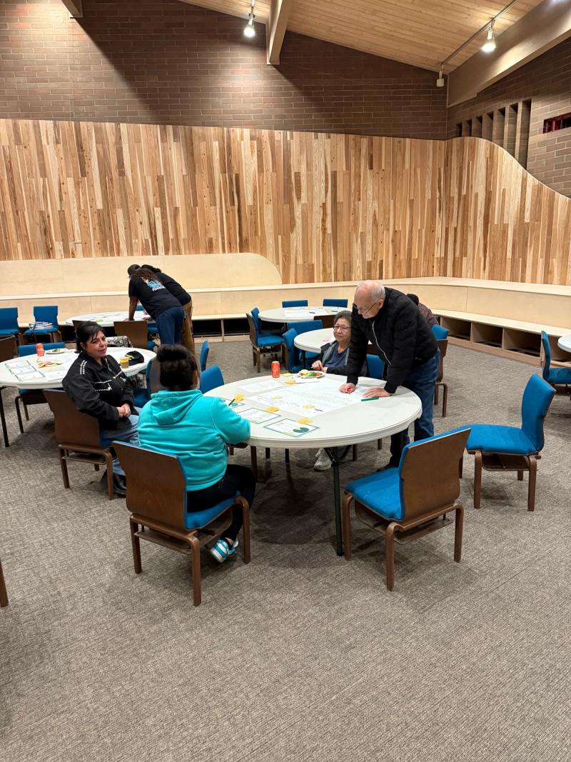 Community members gather at round tables in the renovated Barbie’s Village hall, with its curved wood wall.