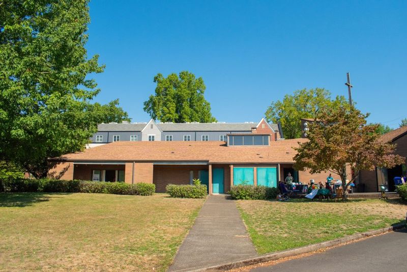 The former Laurelhurst Presbyterian Church: a low brick building set back behind a lawn and mature trees, under a clear sky.