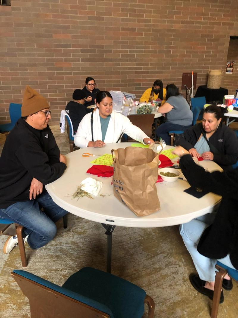Caregivers sit around a table making crafts together in a brick-walled community room.