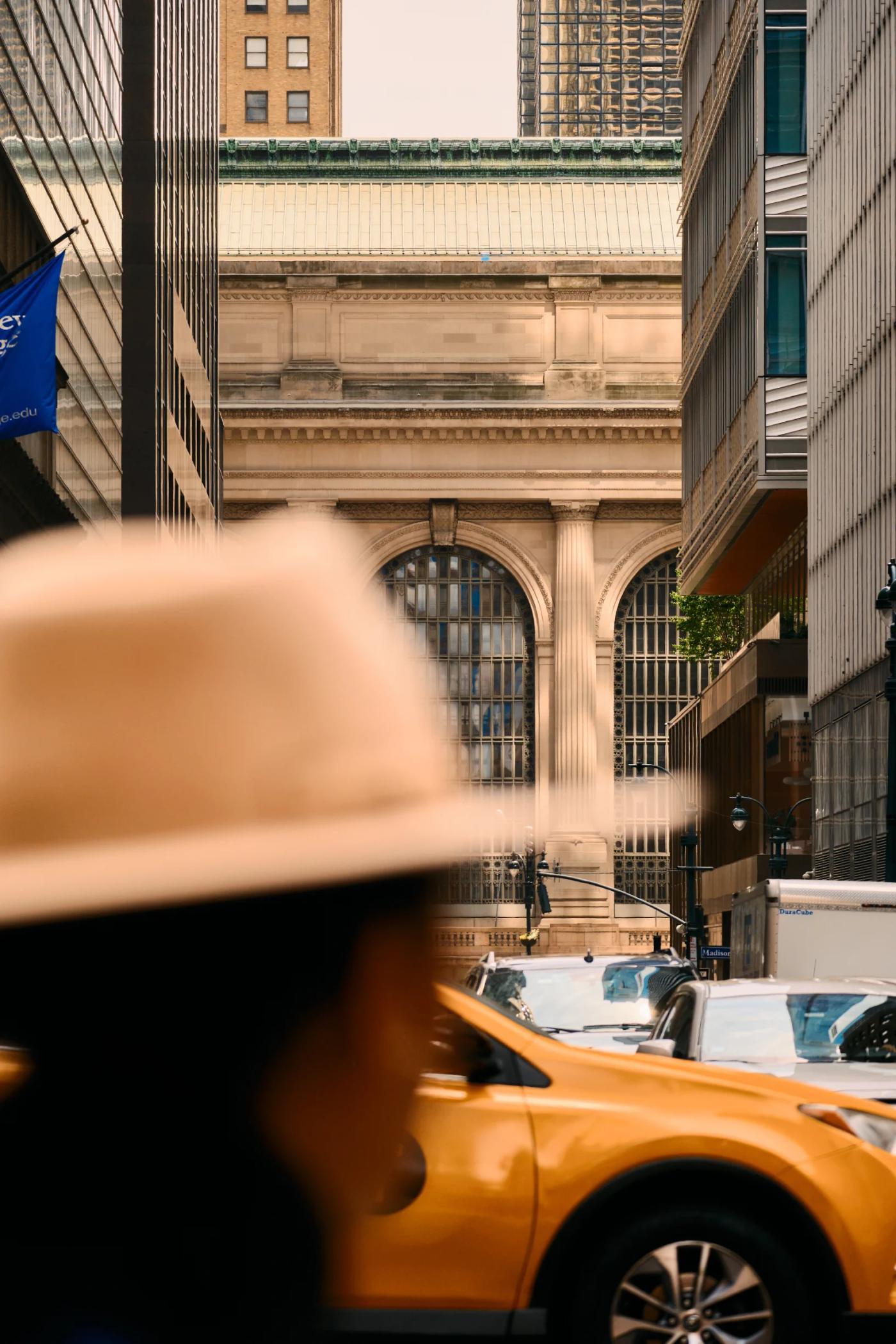 A bustling city street with tall buildings, parked cars, and a yellow taxi.