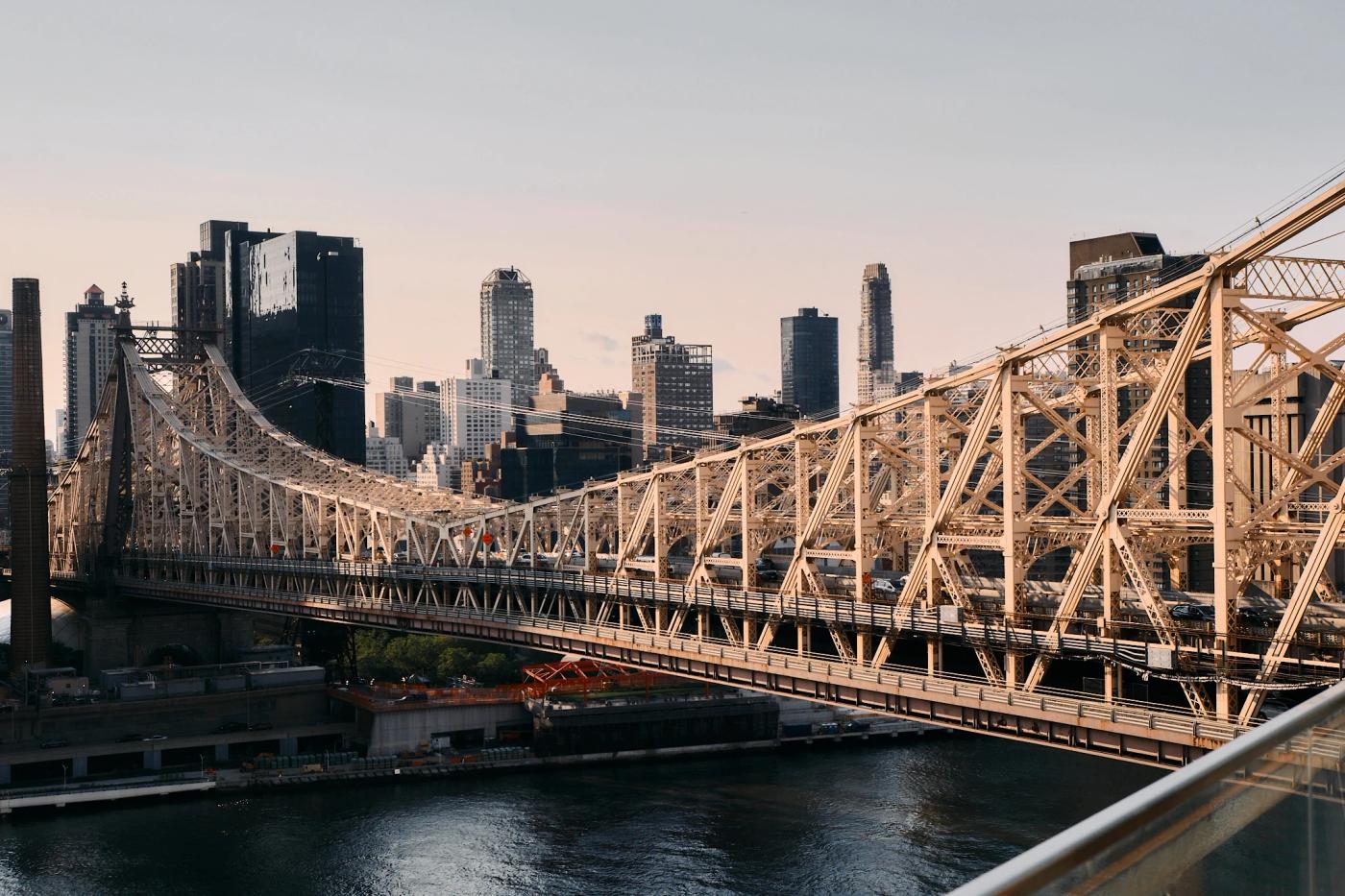 The image features the Brooklyn Bridge in New York City, with a light-colored steel cable bridge spanning the East River. The city skyline, including 