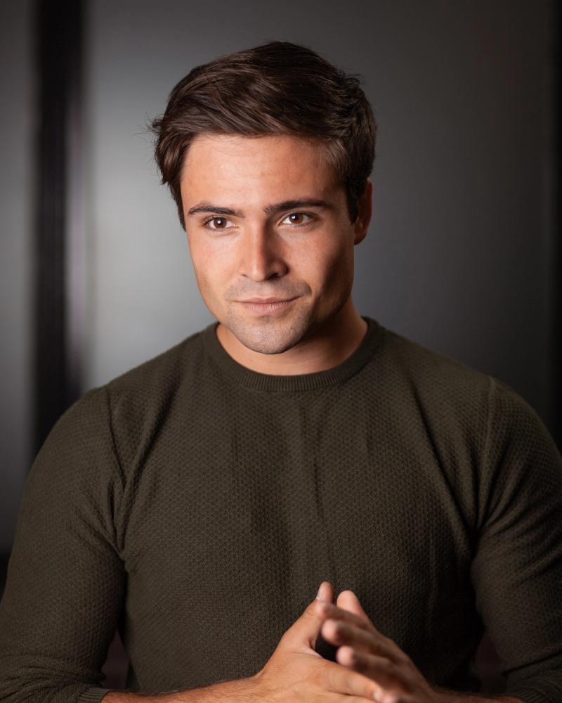 Studio portrait of a man in a dark shirt with hands clasped