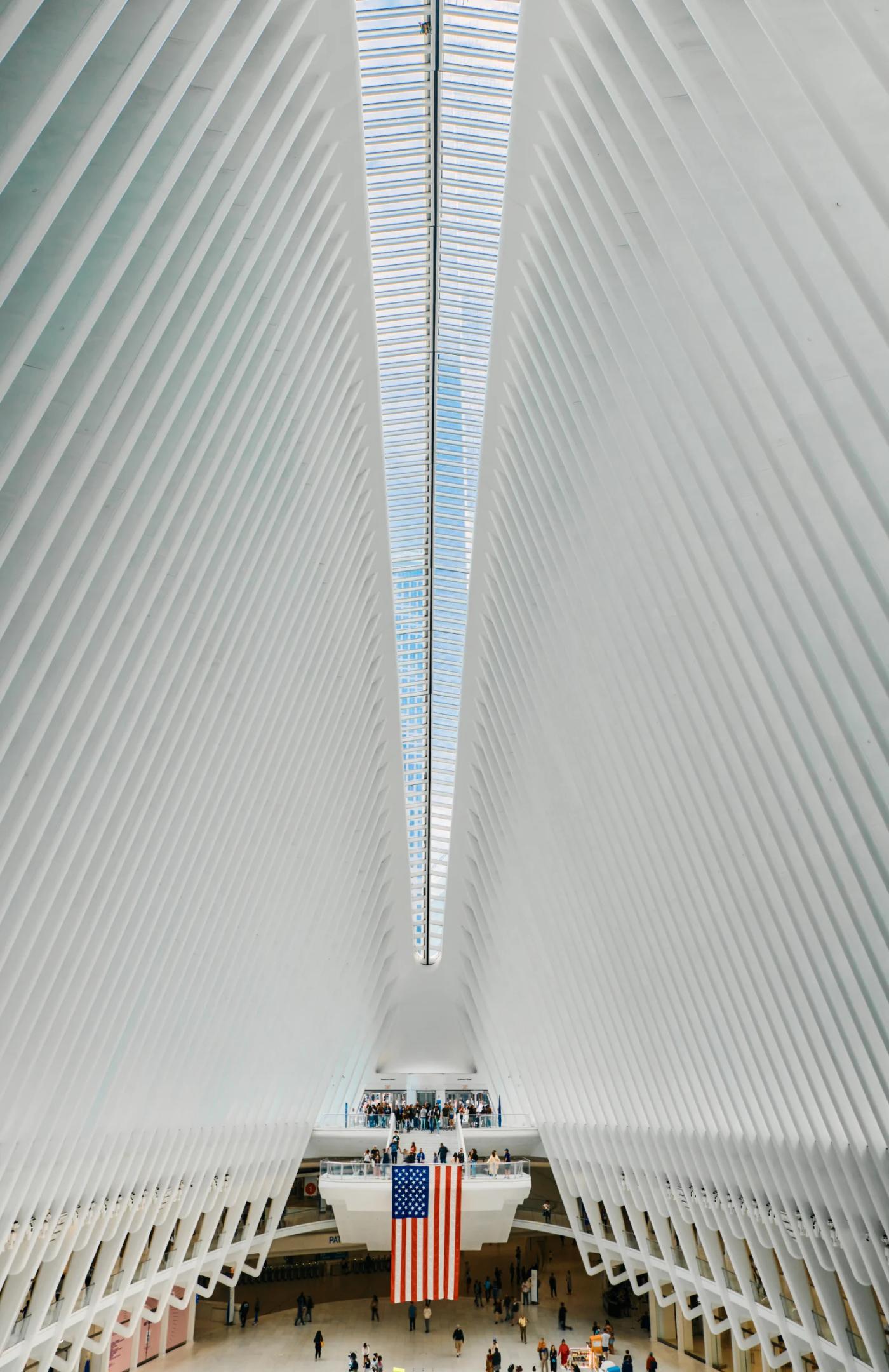 A bustling train station with a large, modern, white ceiling and a large American flag hanging from the ceiling.