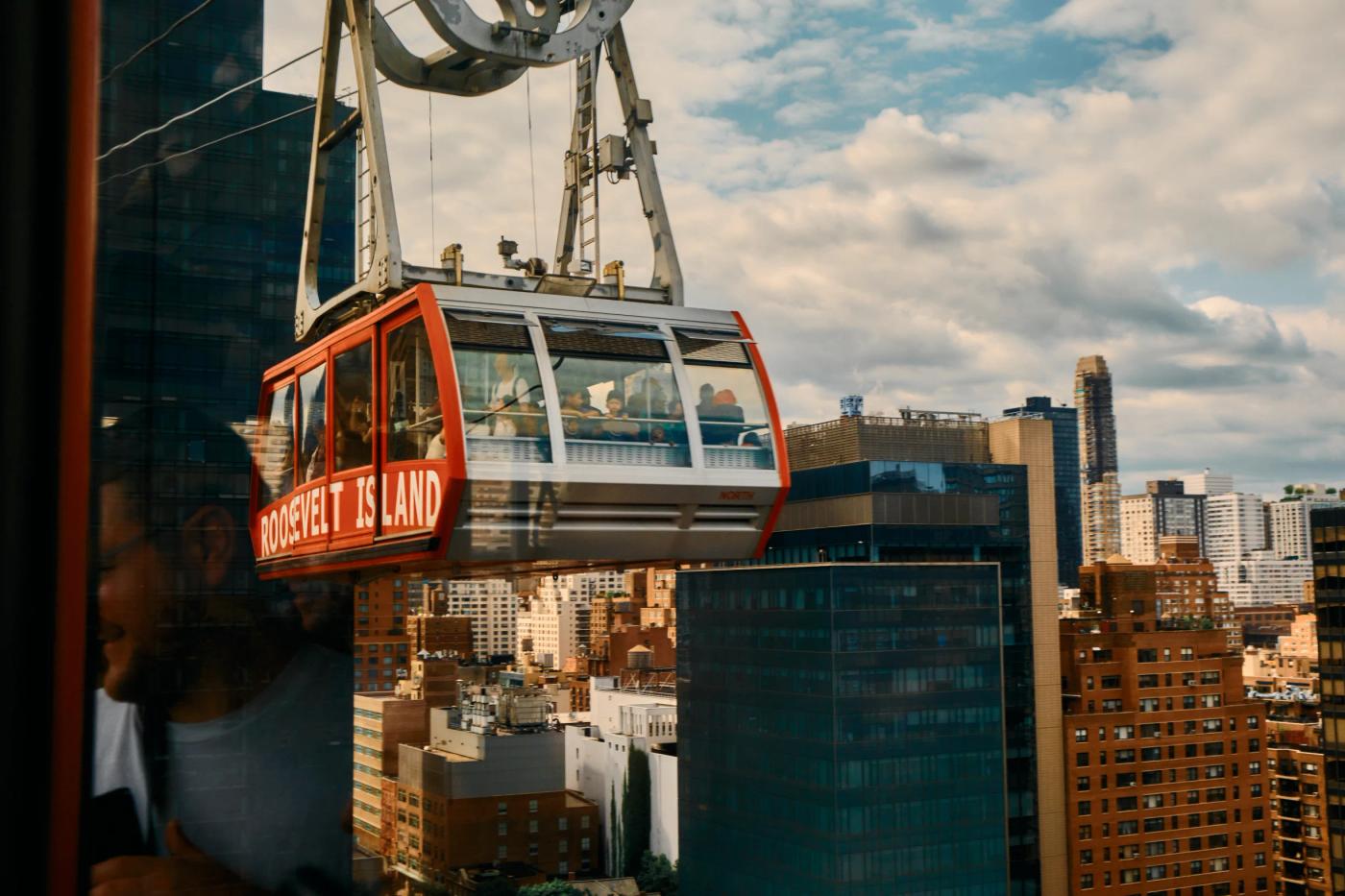 A red and white cable car with "CITY CABLE" written on it is suspended in the air above a bustling cityscape. The cityscape features tall buildings, a