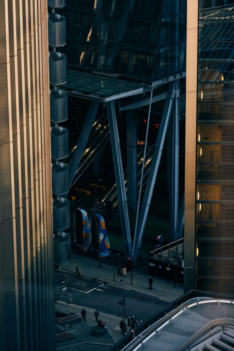 Modern commercial courtyard with blue steel X-frame structural beams between glass office buildings at golden hour, City of London