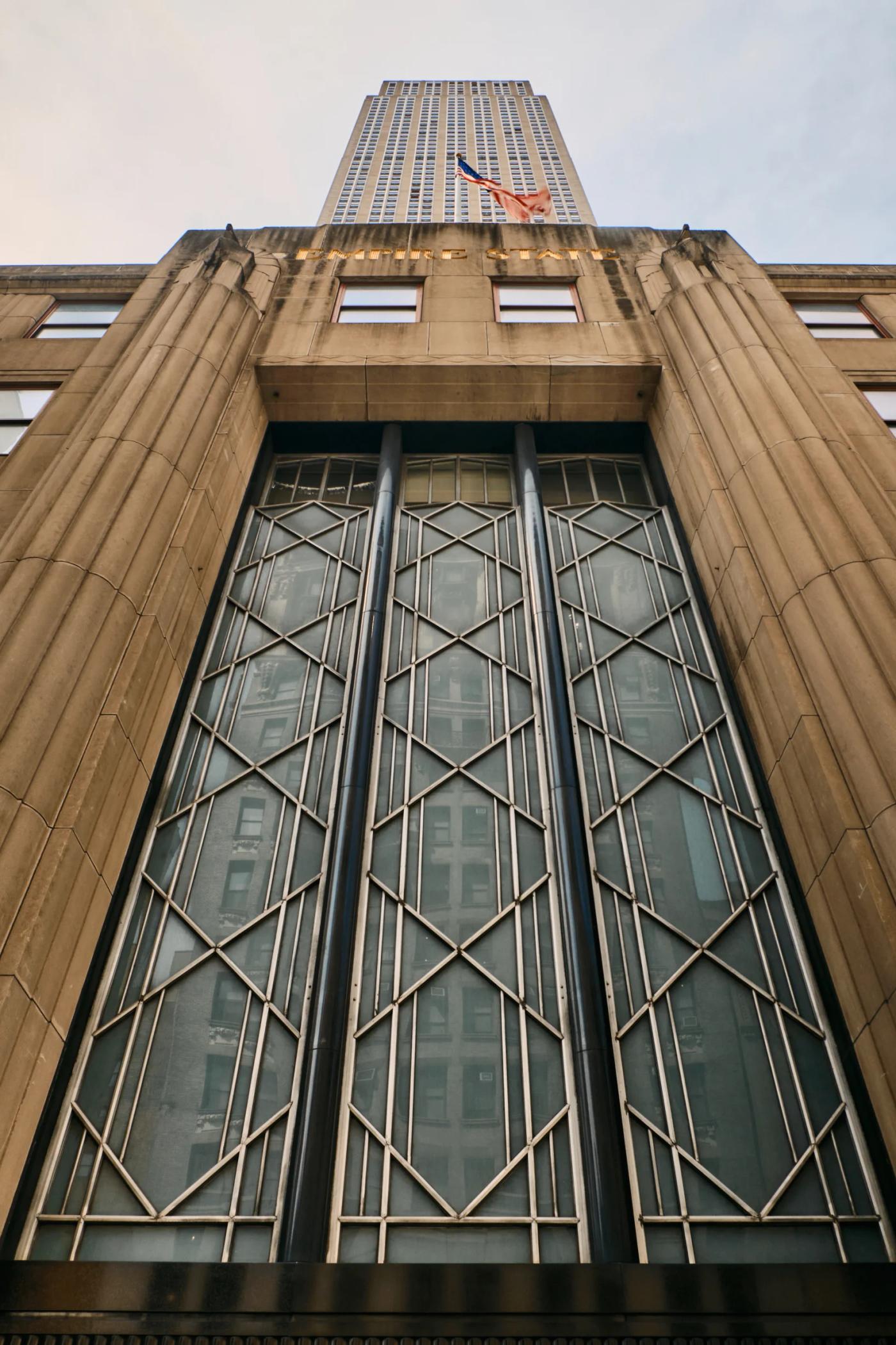 The image features the iconic 100 Rockefeller Center skyscraper in New York City, with a low-angle perspective emphasizing its height and grandeur. Th
