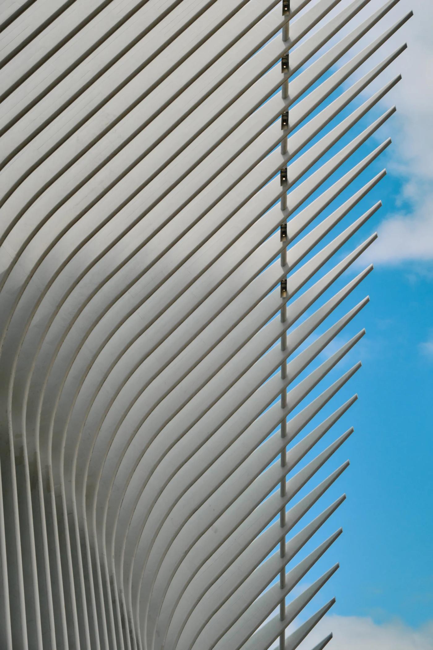 A modern, curved white building with horizontal slats and vertical bars is captured in a low-angle shot, showcasing its unique design.