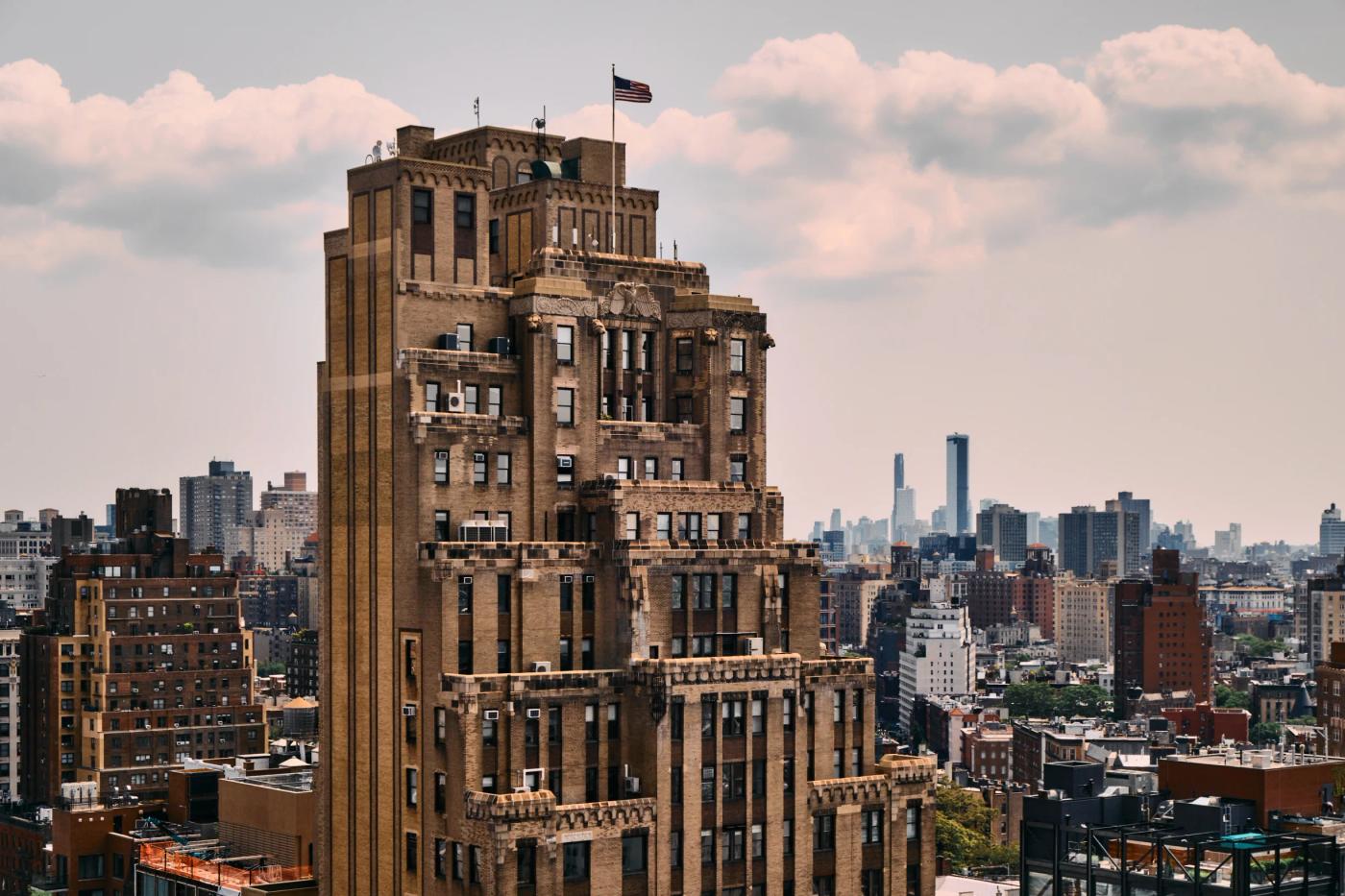 The Empire State Building in New York City is captured from a high vantage point, showcasing its brown facade and intricate details. The American flag