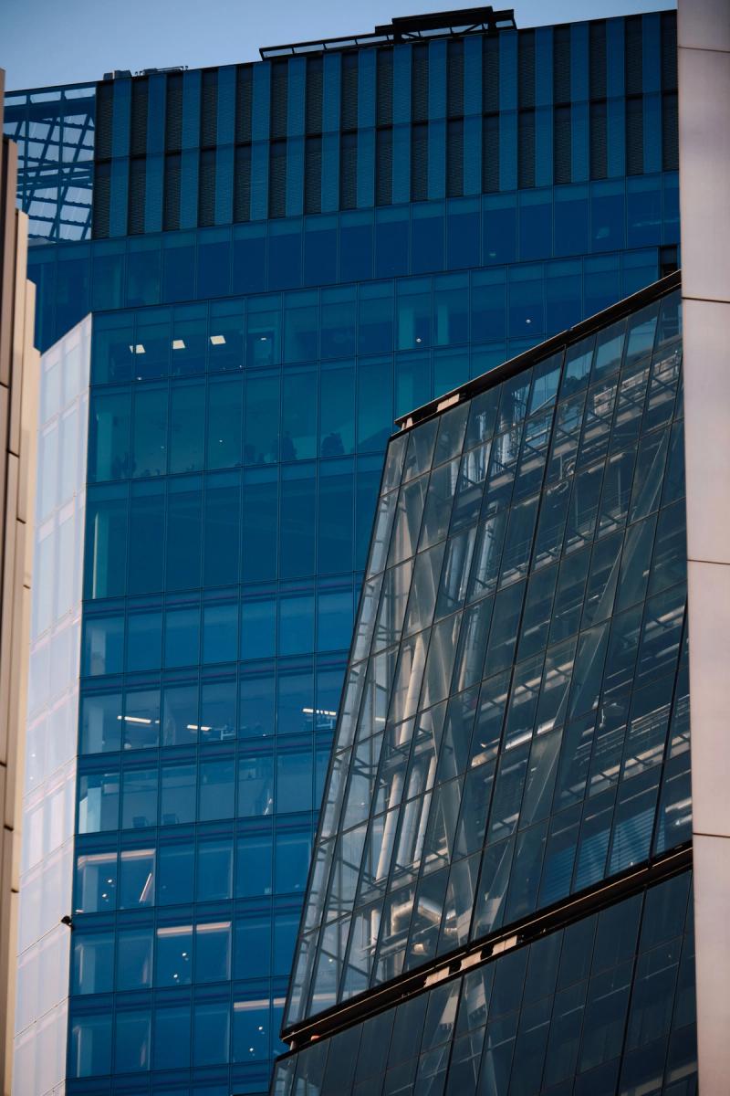 Contemporary glass office building facade with teal-blue reflective curtain wall, vertical metal louvers and angled glass panel section