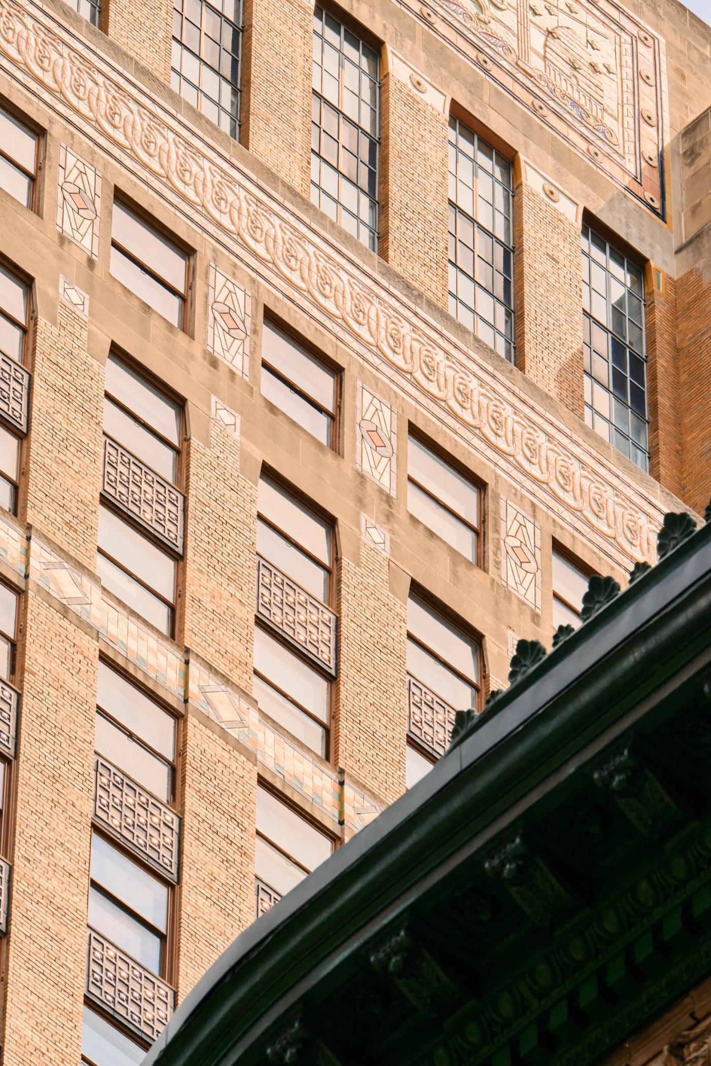 A brick building with rectangular windows and decorative patterns, a green roof, and a low-angle perspective.