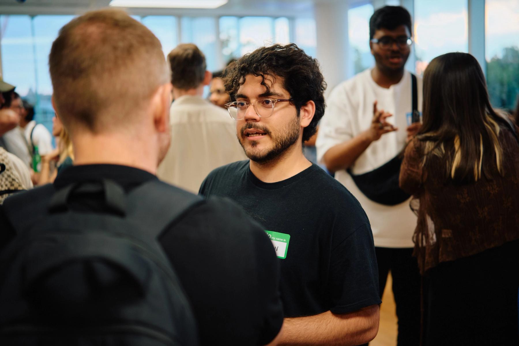 Access VFX community event 2026, attendee with curly hair, glasses, and a name tag mid-conversation in the crowded room
