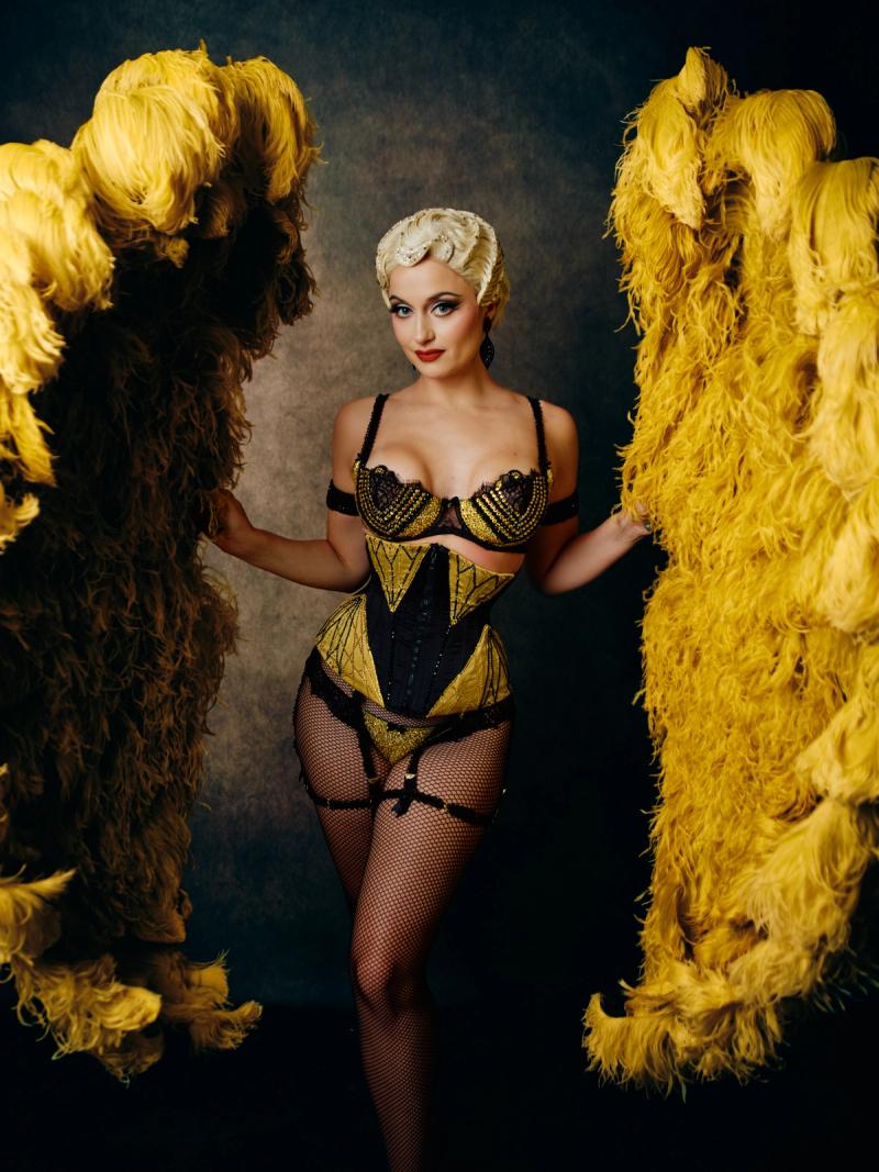 Model posing in a structured gold gown against a textured studio backdrop