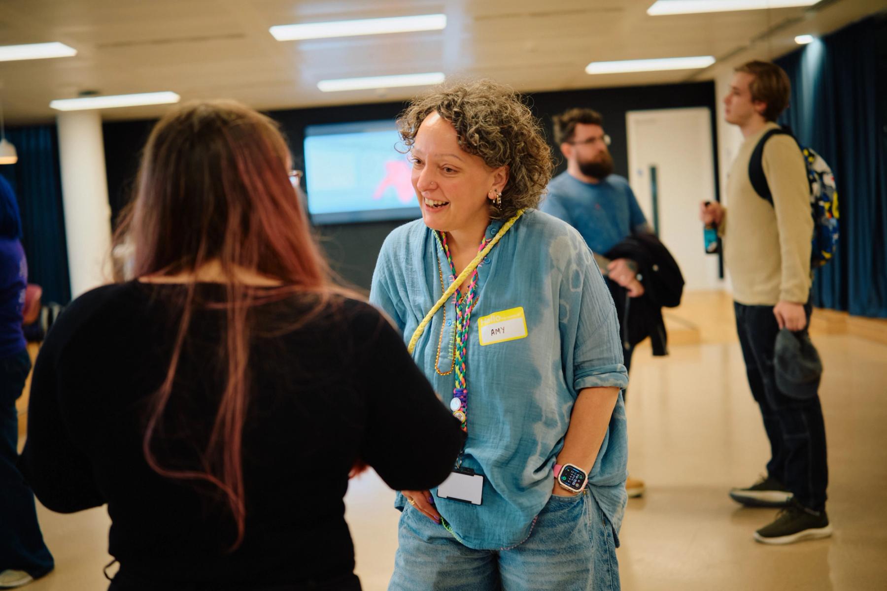 Access VFX community event 2026, Amy in a light blue shirt and yellow name tag smiling while talking to another attendee