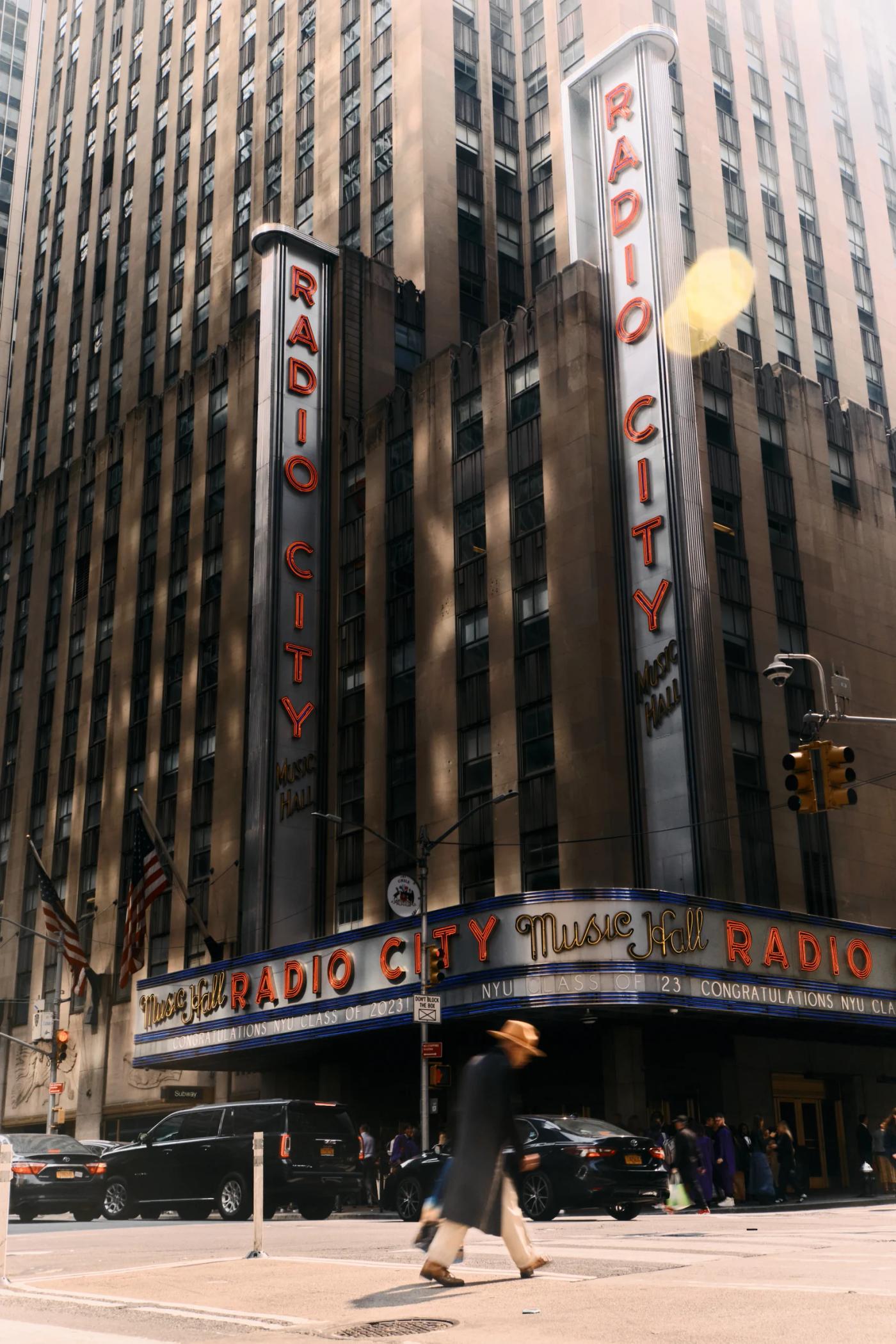 The image captures the iconic Radio City in New York City, featuring the iconic "Radio City" sign, two tall, slender pillars, and a marquee displaying