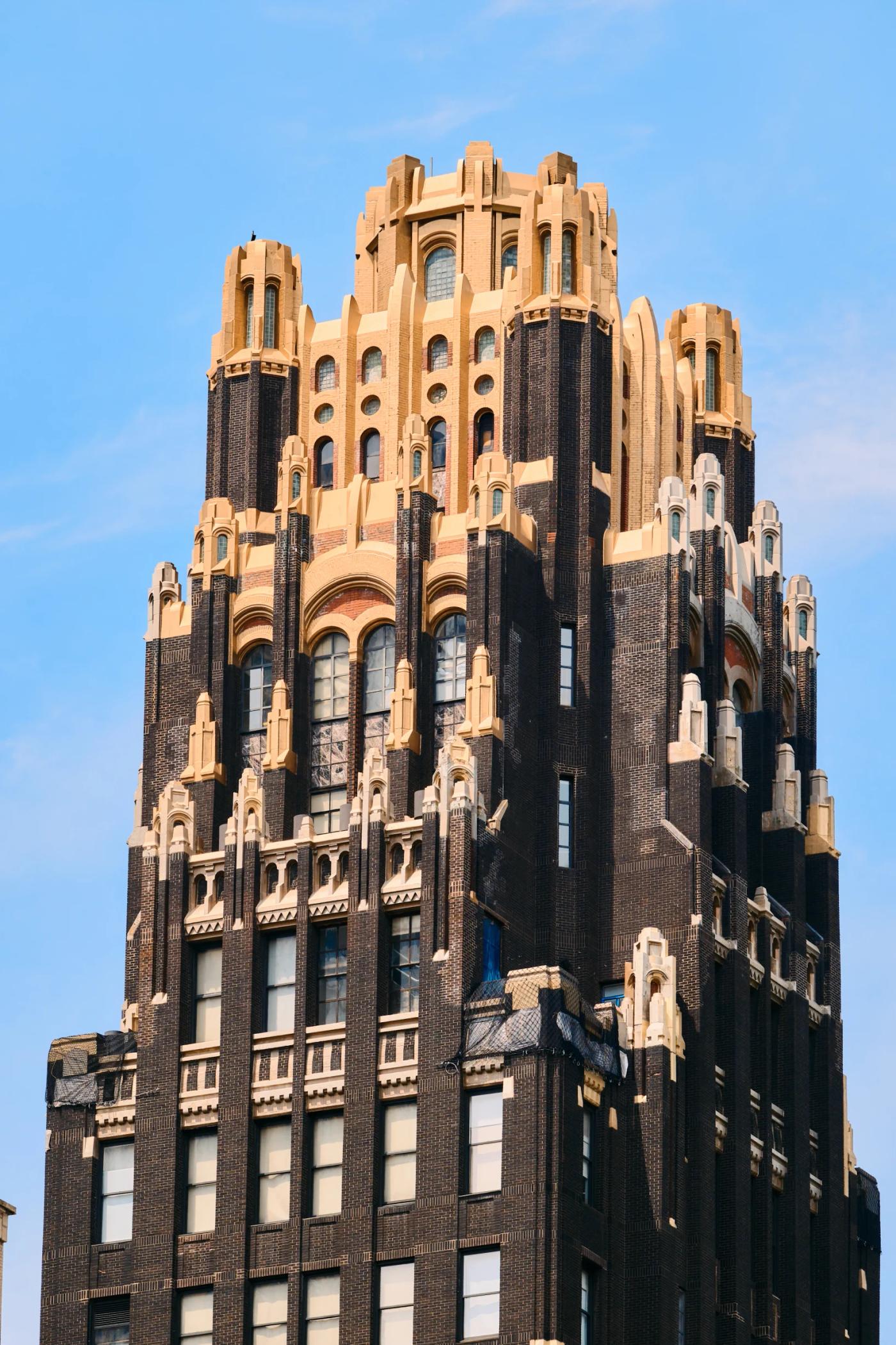 A tall, dark brown building with arched windows and a golden-topped spire stands against a clear blue sky.