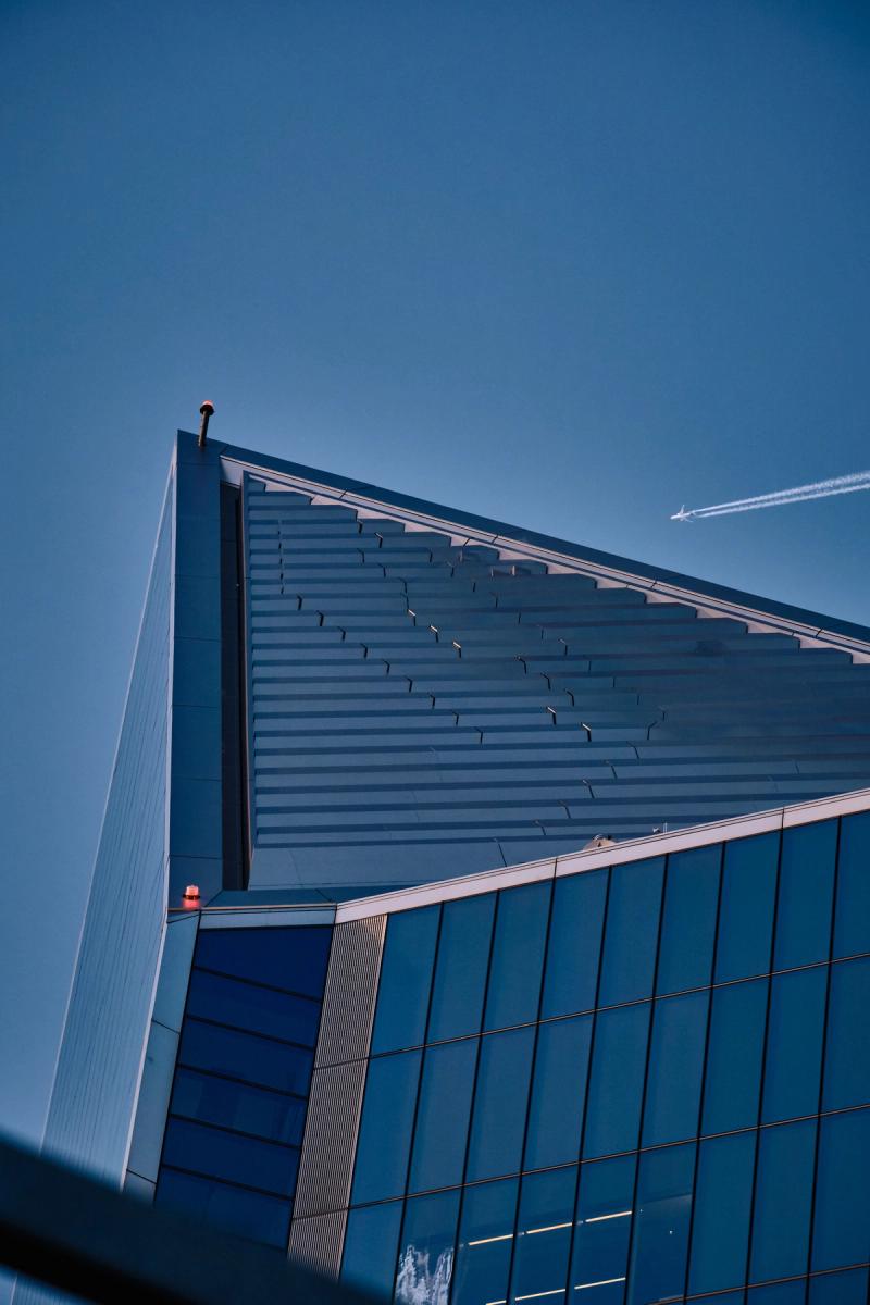 Modern commercial building with angled metallic roof and blue-teal corrugated metal facade, low-angle architectural photography against clear blue sky