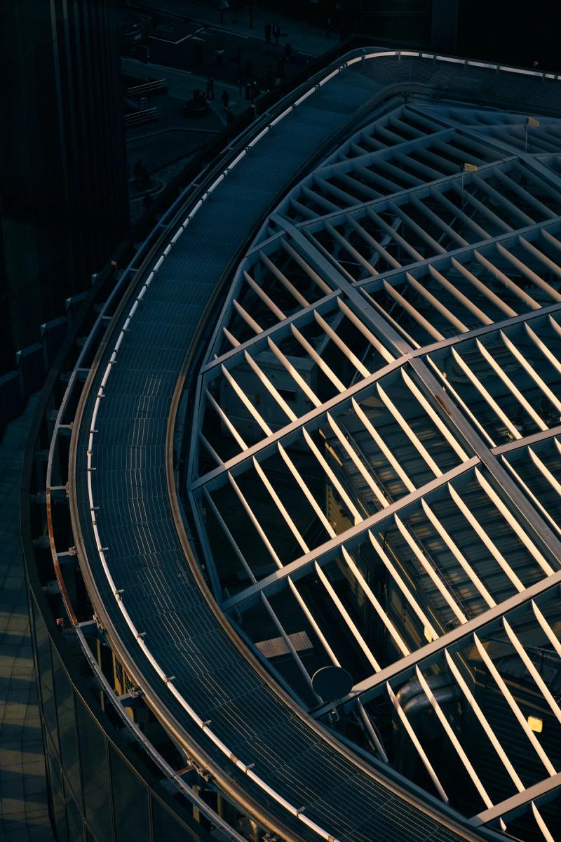 Aerial view of circular modern building with exposed steel beam framework and ribbed metal roof, golden hour architectural photography