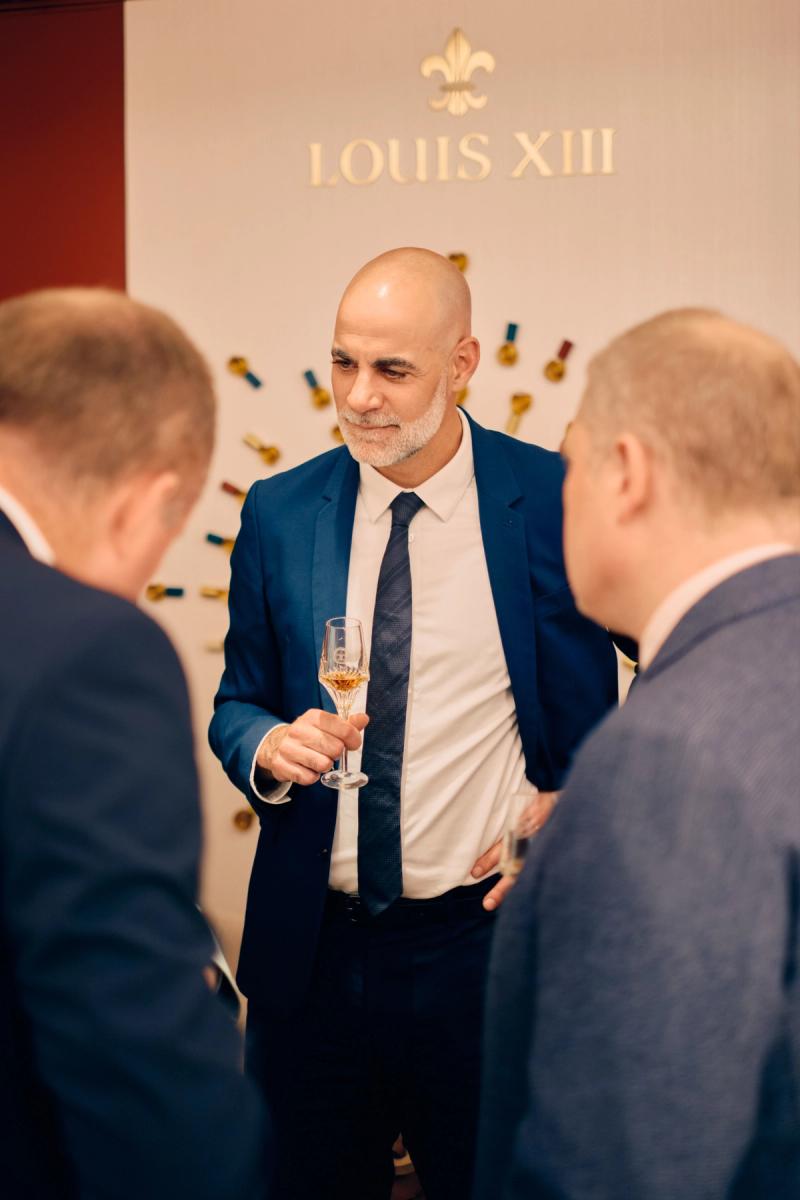 Man in a blue suit speaking with guests during a formal wedding event